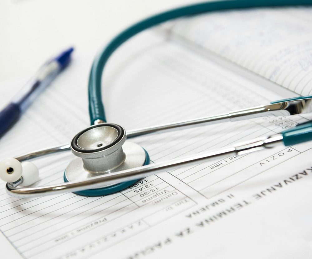 A stethoscope and pen resting on a medical report in a healthcare setting.